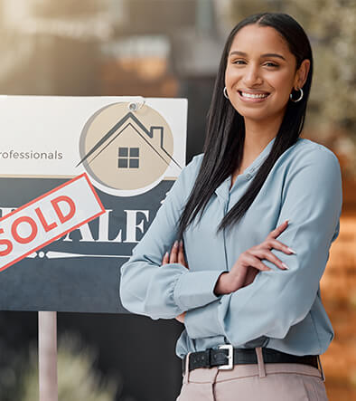 smiling real estate agent standing in front of a SOLD sign